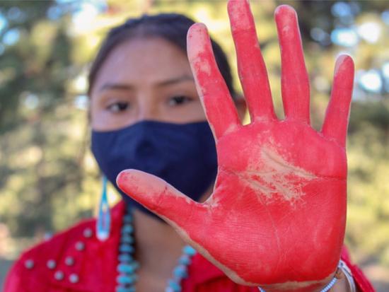 A Native woman holds up her red-painted hand