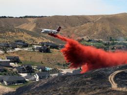 A plane dropping fire retardant ahead of a fire burning near a golf course