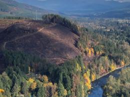 A communications tower sits on top of a burned hillside in a forest next to a river