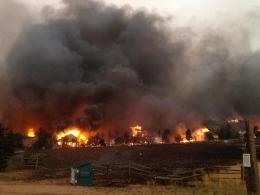 Wildfire burning a residential area behind a wooden spilt-rail fence