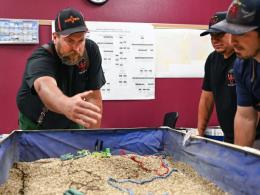 Wildland firefighters conduct a training exercise using a sand table to emulate an active wildfire situation. 