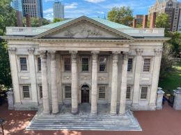 A building with marble facade with six columns and steps leading to front door. A large carved eagle is on the the building's triangular pediment above the columns.