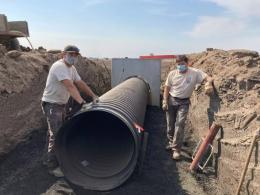 Two MAT workers stand next to a large pipe next to dirt walls