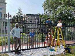 Four people standing along an iron fence. Two people are standing on ladders.