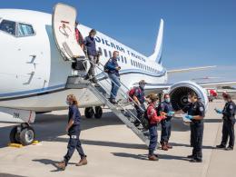 Firefighters exiting an airplane are greeted by U.S. customs agents on the tarmac