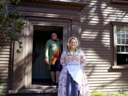 Two park rangers in historic colonial American dress smile outside a historic house