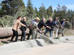 Seven people, one in park ranger uniform and six in office wear, break ground with shovels in forest 
