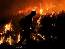 A silhouetted firefighter uses a drip torch at night. Flames rise from vegetation that looks black in the night. Photo by Austin Catlin, BLM.