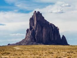 Steep pointed rock formation in desert landscape. 