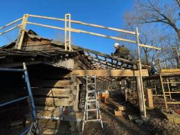 Worker in safety gear putting new wooden roof on a log barn with a bright blue sky in the background