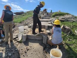 Montana Conservation Corps team members work on trail stairs that lead up a grassy hill