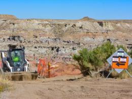 Construction machinery on a sandy landscape with orange fencing and signs