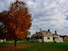 White building with shingle roof among fall colored trees.