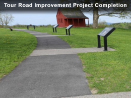 Paved path surrounded by green grass with interpretive displays leads to red building