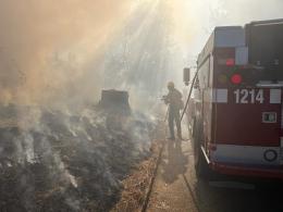 A firefighter sprays water on a wildfire as he walks next to a red fire engine. 