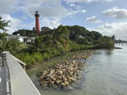Photo is taken from an overlook of a waterway with a rocky shore and a red lighthouse in the background