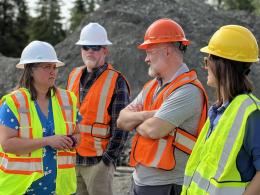 Four people in safety vests and hard hats talk to each other.