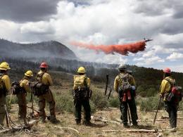 Six wildland firefighters watch an airtanker drop red retardant on a fire.