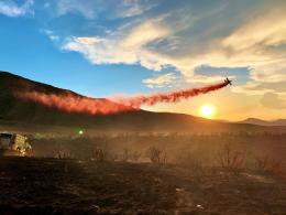 An airtanker drops red retardant on a wildland fire at sunset