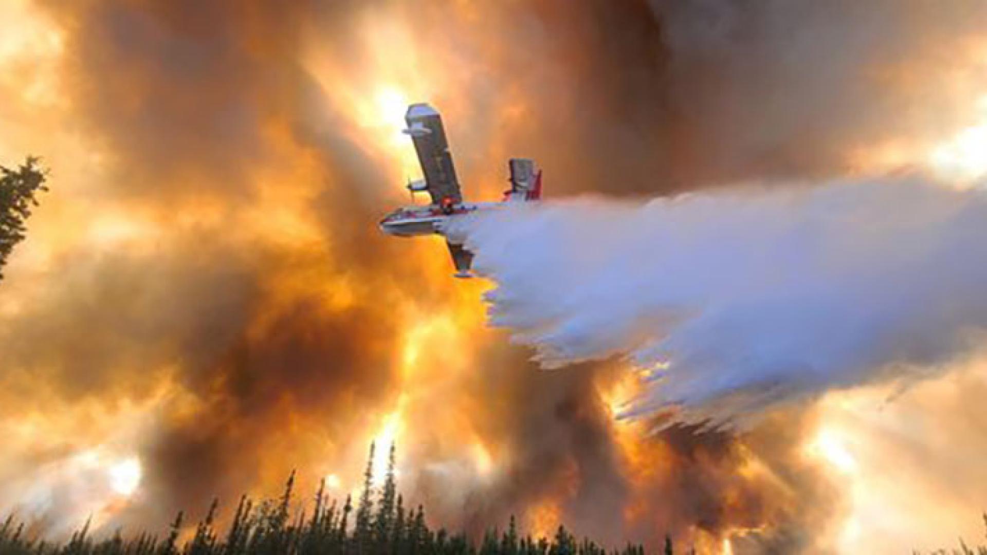 A plane seen from below dropping water on the Clear Fire in Fairbanks, Alaska, against an orange, smoke-filled sky. Photo by Eric Kiehn, Kittitas County Fire District 1.