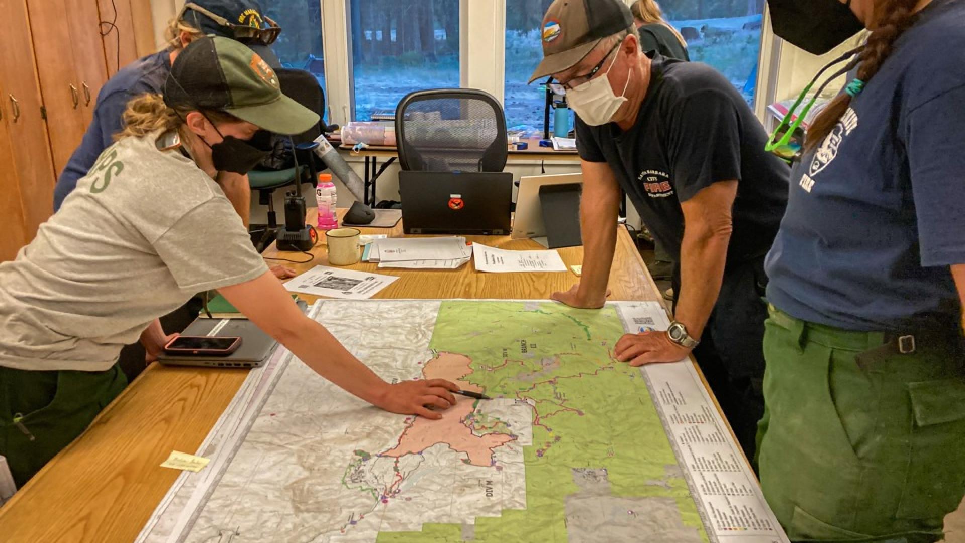 Wildland fire resource advisors study a map showing the outline of a wildfire and the surrounding area during a briefing. Photo by Cedar Drake, NPS.