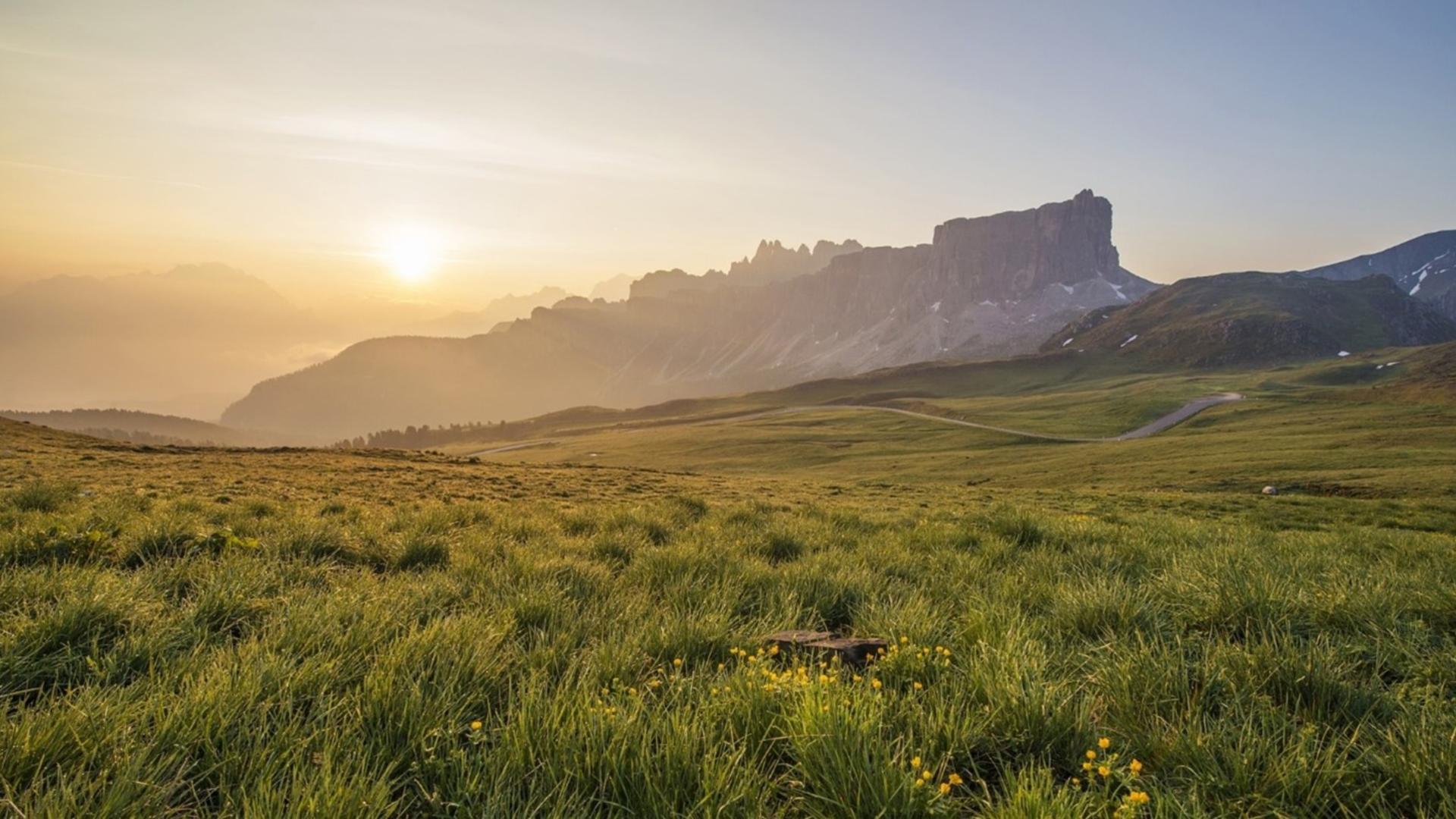 Image of green field with sunrise and rock formations in background.