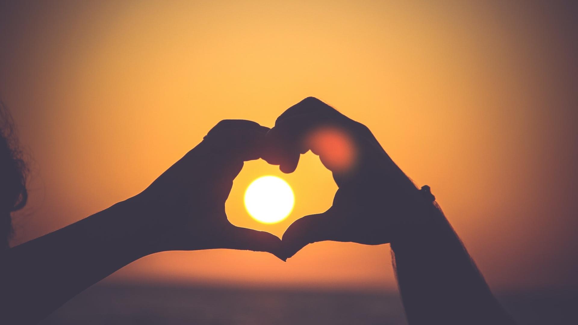 Picture of two hands making a heart at sunset
