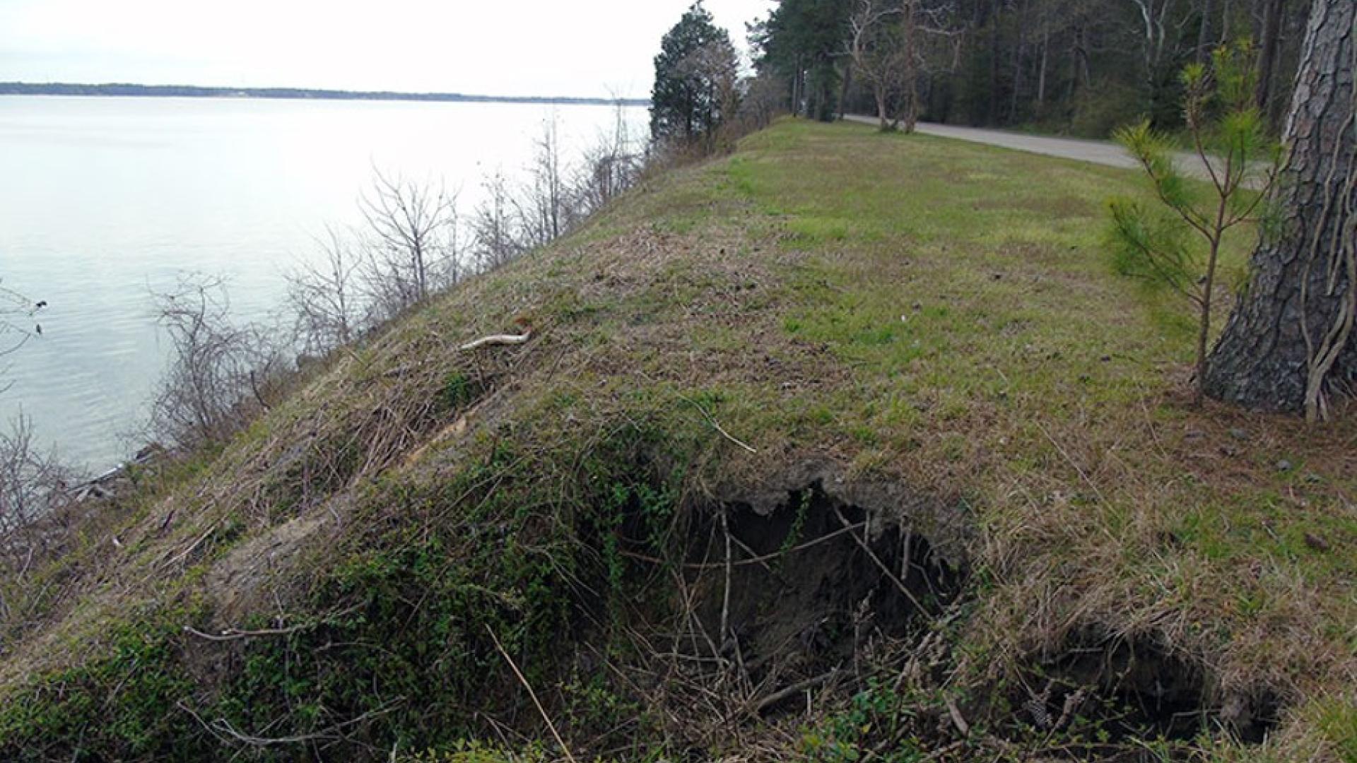 Shoreline erosion of grassy hillside along a paved road and a waterway 
