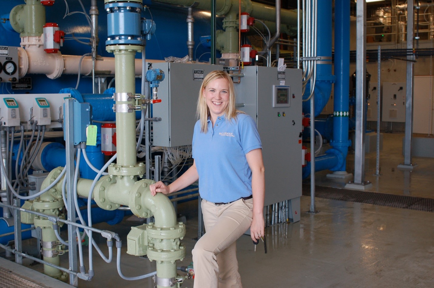 Dani smiles in front of water reclamation equipment. 