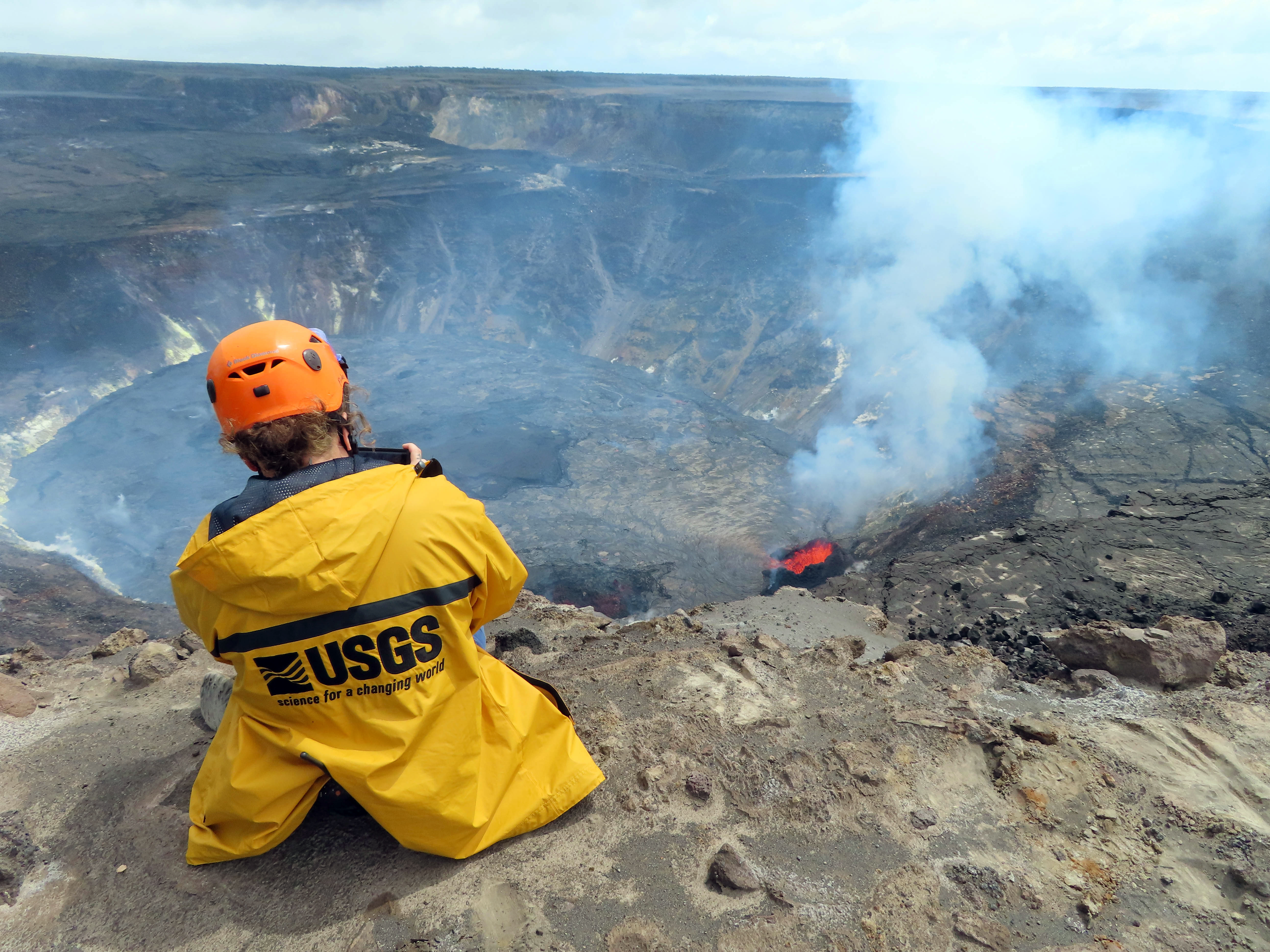 Scientist studying volcano from a cliff ledge. 