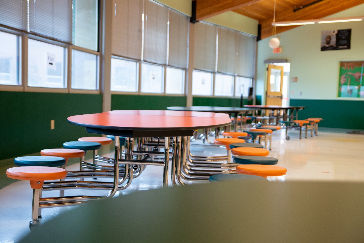Tables and chairs sit in a cafeteria.