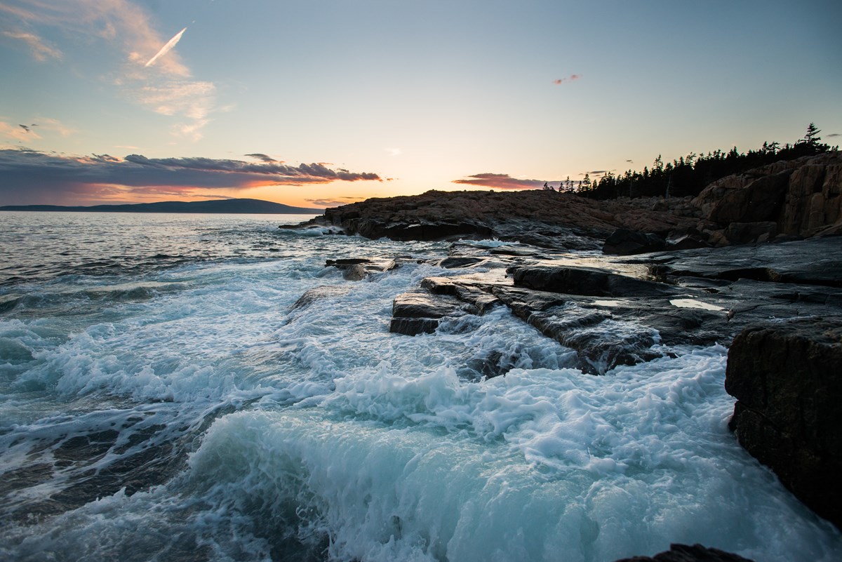 Waves crashing over a rocky coastline at sunset.