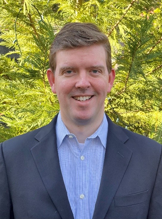 Portrait of Drew Wallace in front of green foliage.