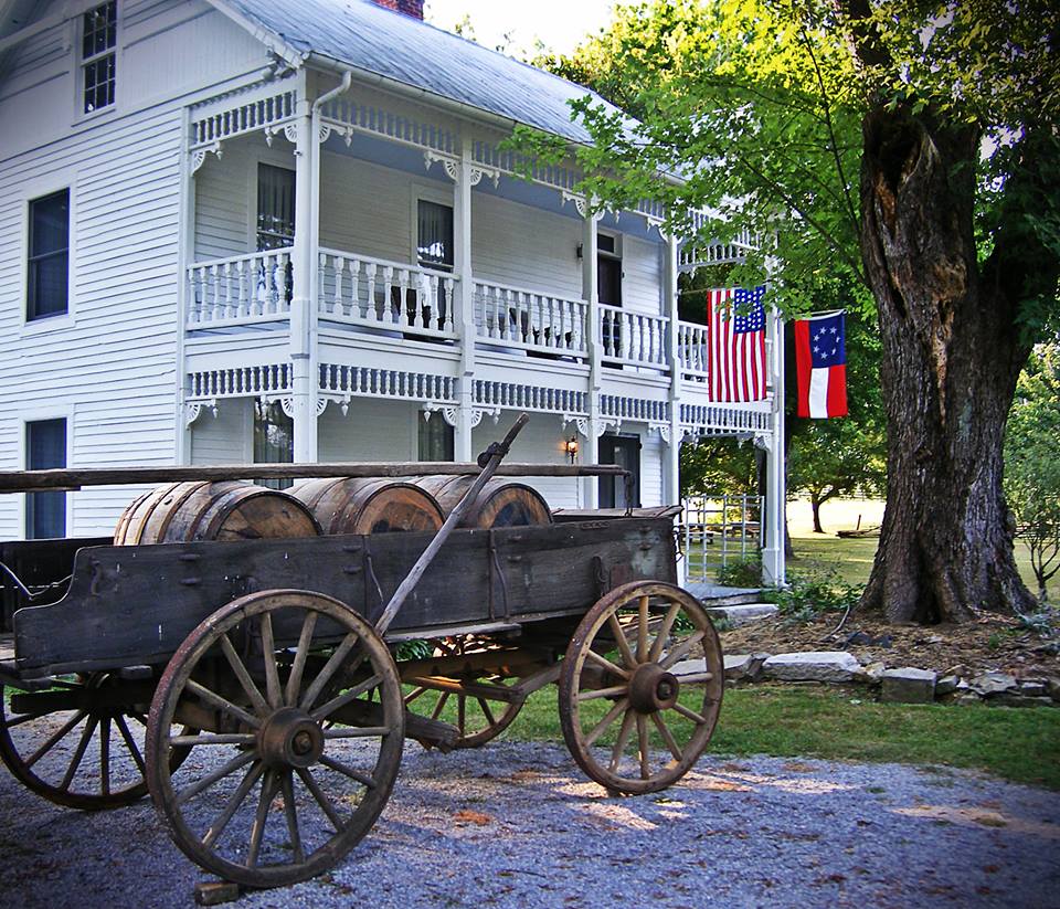 A wooden wagon stands in front of an old white wooden house.