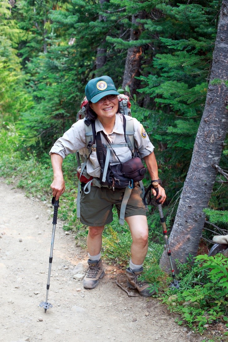 Volunteer stands and smiles on the trail while holding walking sticks.