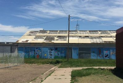 A blue school building with graffiti and a fence around it, badly in need of roof repairs