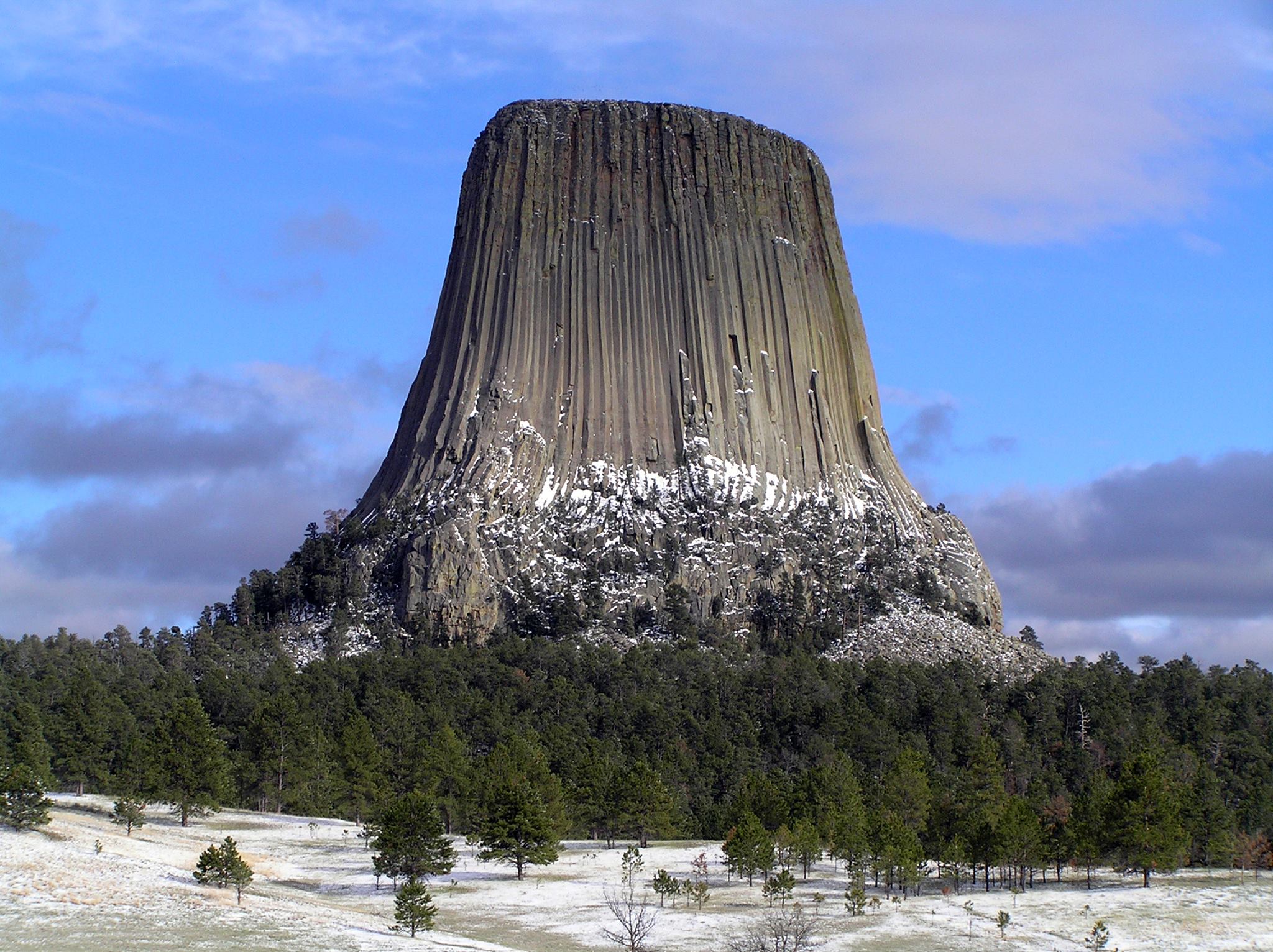 A large natural rock tower with vertical groves rises above a hill covered in trees.