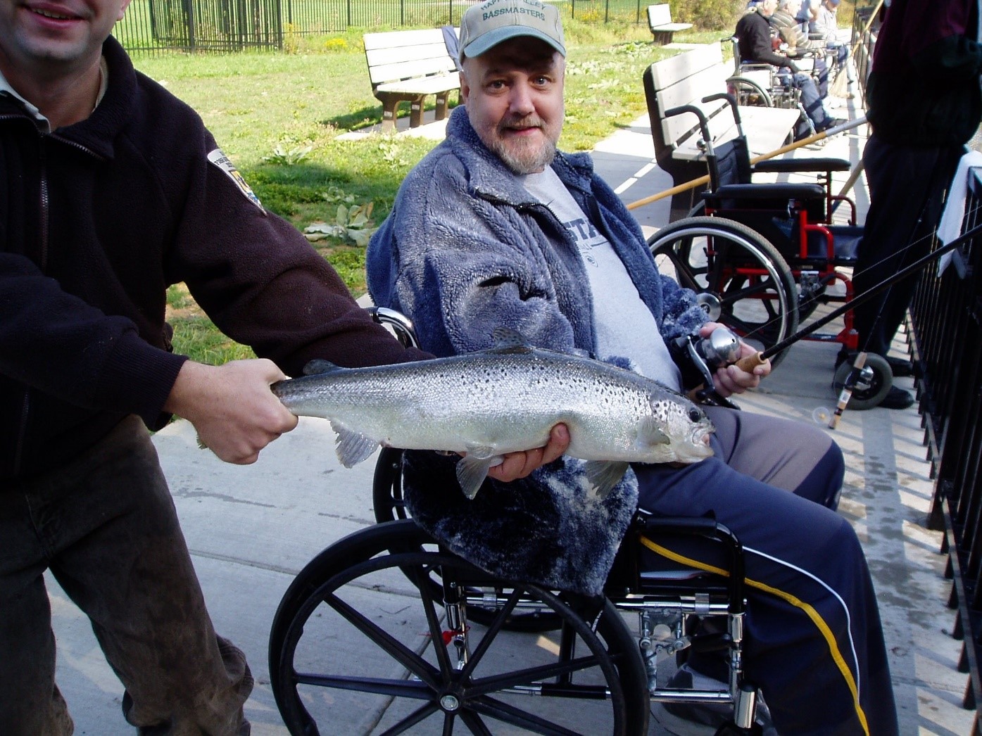 Fishing Day participant holds a silver, glimmering fish in front of another participant