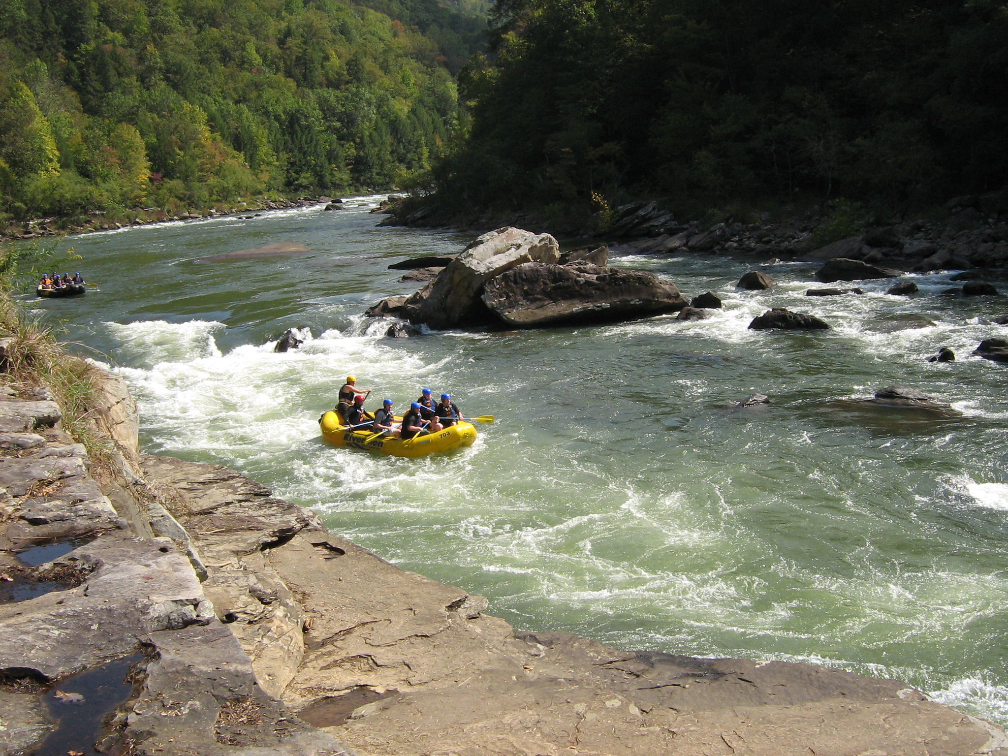 People paddle down rapids in yellow inflatable rafts.