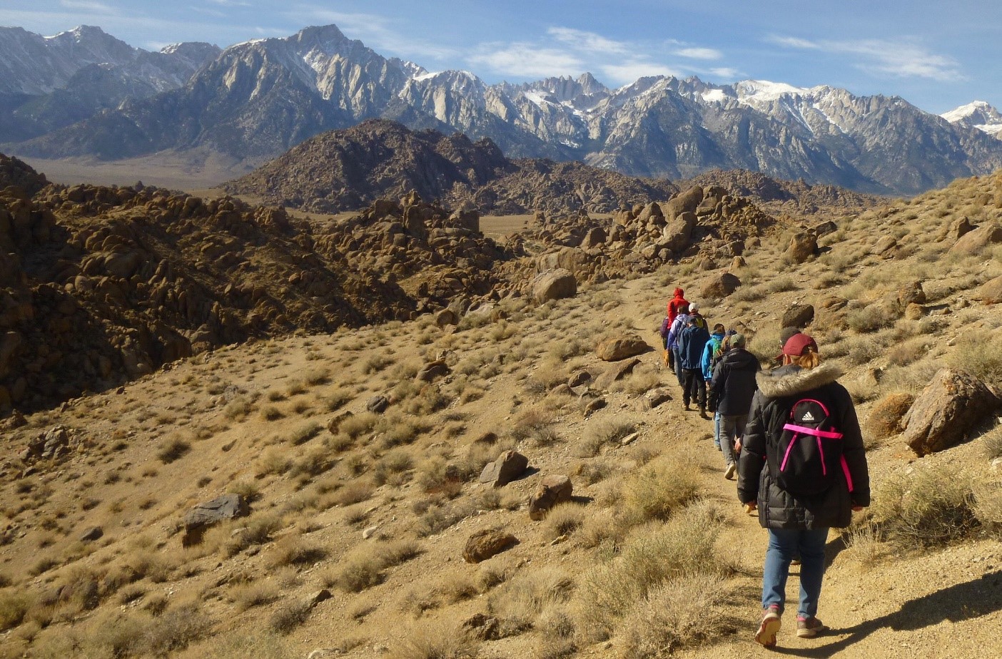 Group of people work toward snow-covered mountains in the distance.