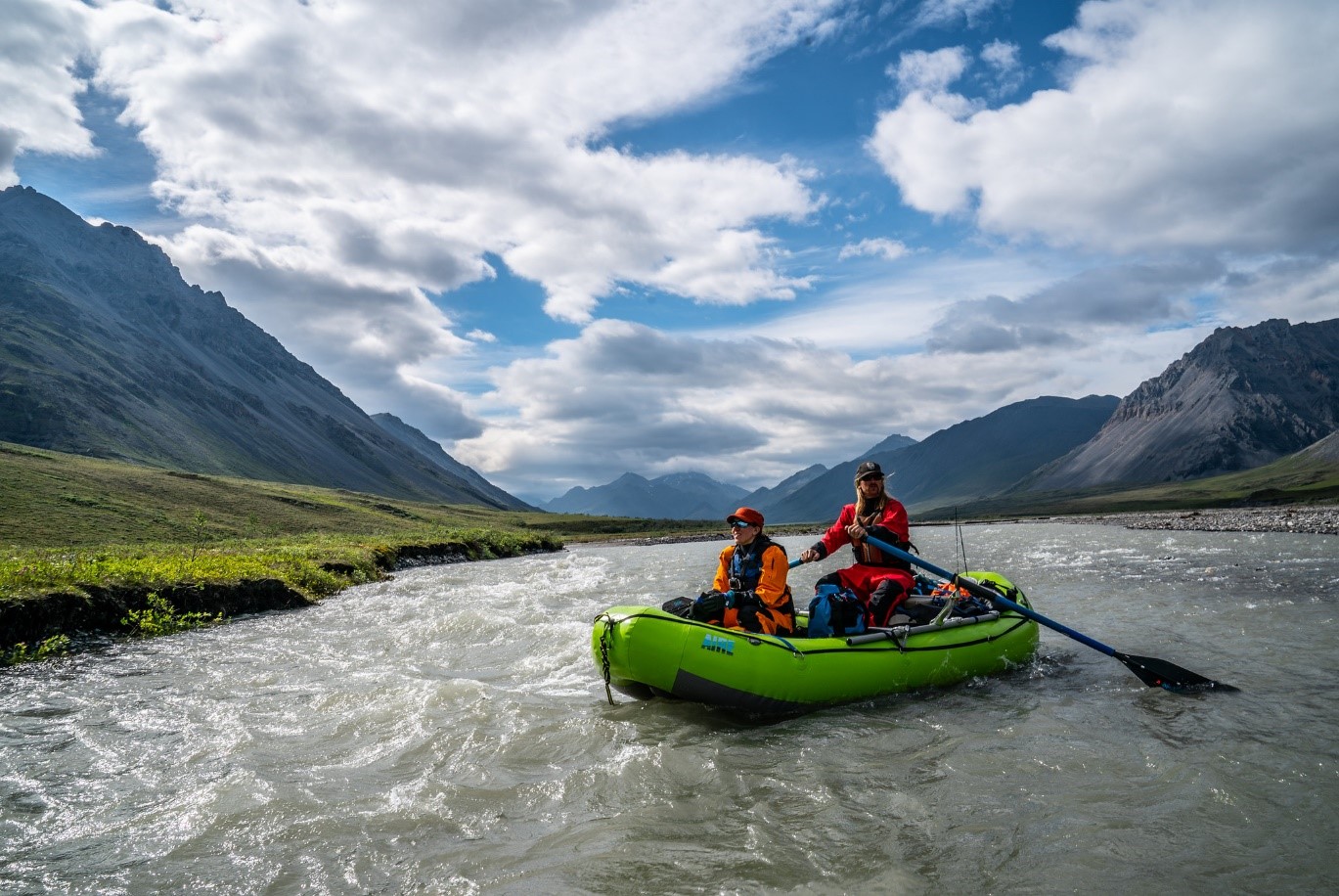 Two people in a raft on the Hulahula River with mountains in the background.
