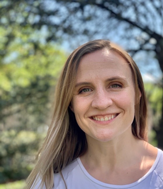 Portrait of Maggie Thompson outside, smiling in front of green foliage.