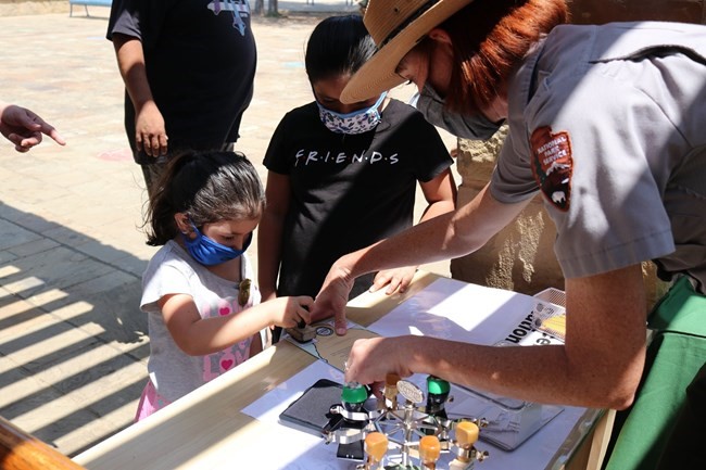 Park ranger in a mask helps a child apply a stamp. 