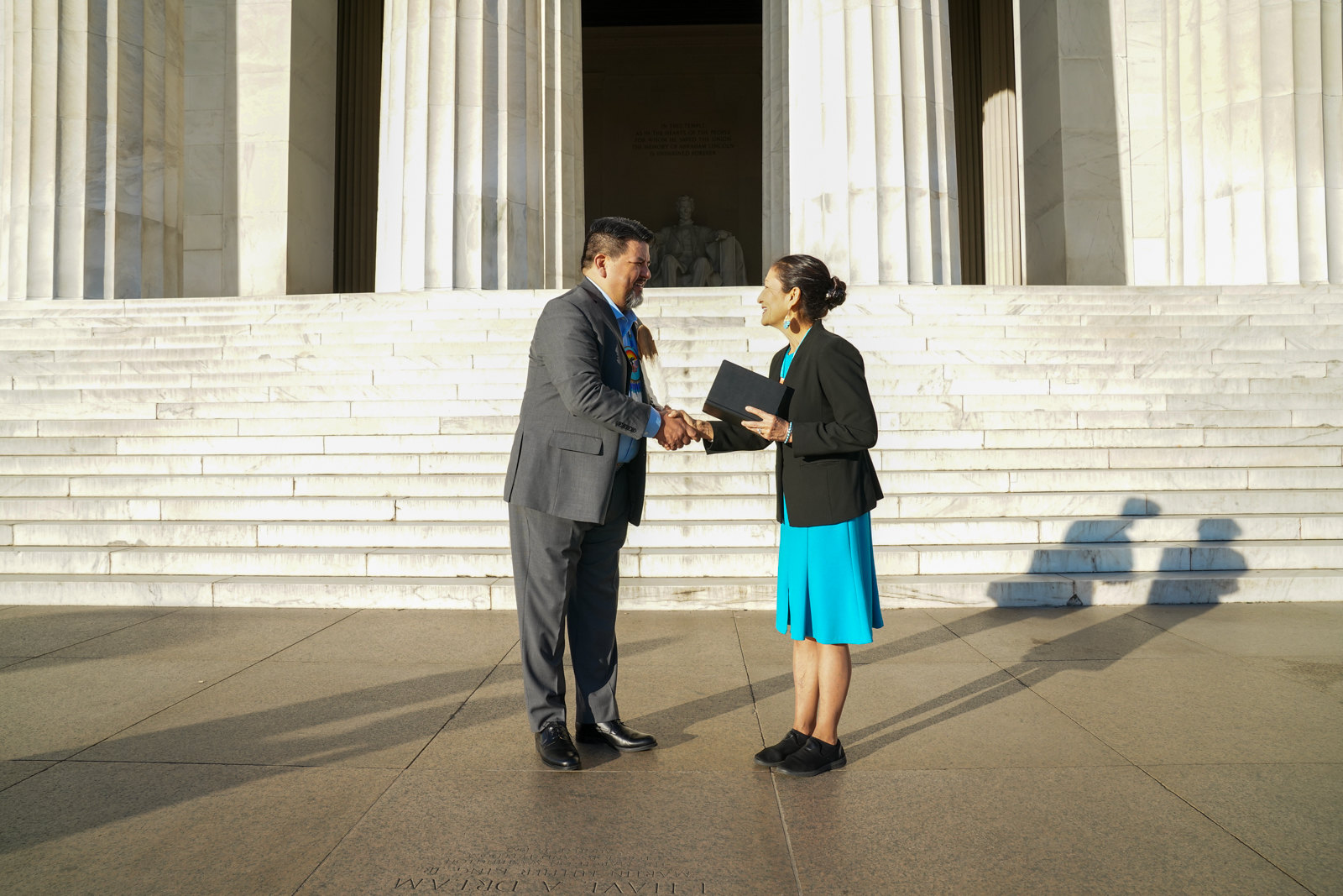 Director Chuck Sams and Secretary Deb Haaland shake hands in front of the Lincoln Memorial.