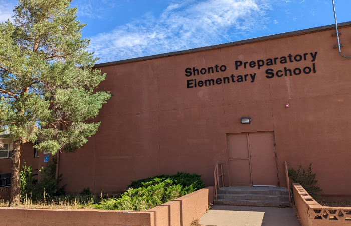 A rust red school building with Shonto Preparatory Elementary School on it in black letters and a tree. 