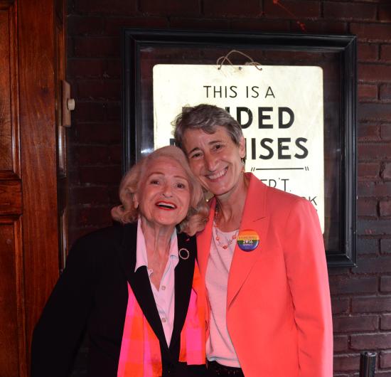 Secretary Jewell smiles brightly while posing for a photo with Edie Windsor. Jewell is wearing a coral blazer with a “Stonewall 2016” pin, and Windsor is wearing a black coat with a pinkish red scarf wrapped around her neck. 