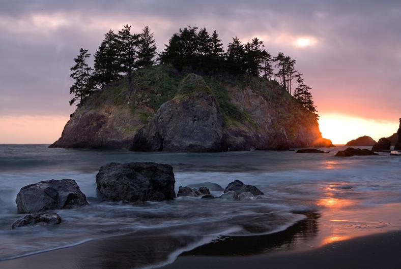 Ocean waves flow onto the sand and rocks of a California beach at sunset.