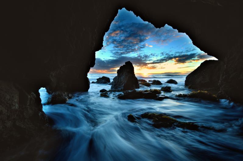 Surf from the Pacific Ocean rushes into a rocky cave on the beach