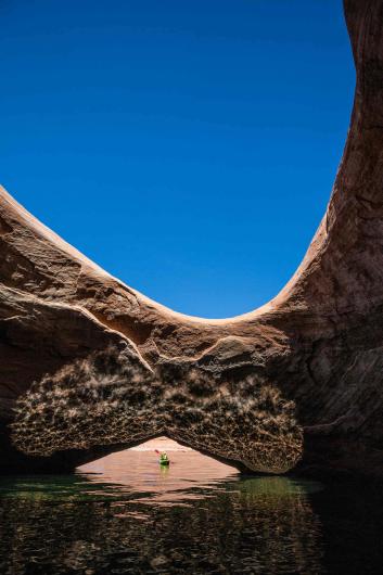 A person in a kayak paddling under stone arch over the water.
