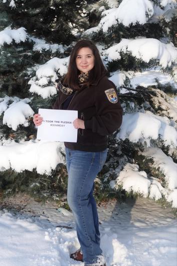 Ana Munoz from USFWS, standing outside by snowy tree, holding the I took the Pledge #DenimDay sign. 
